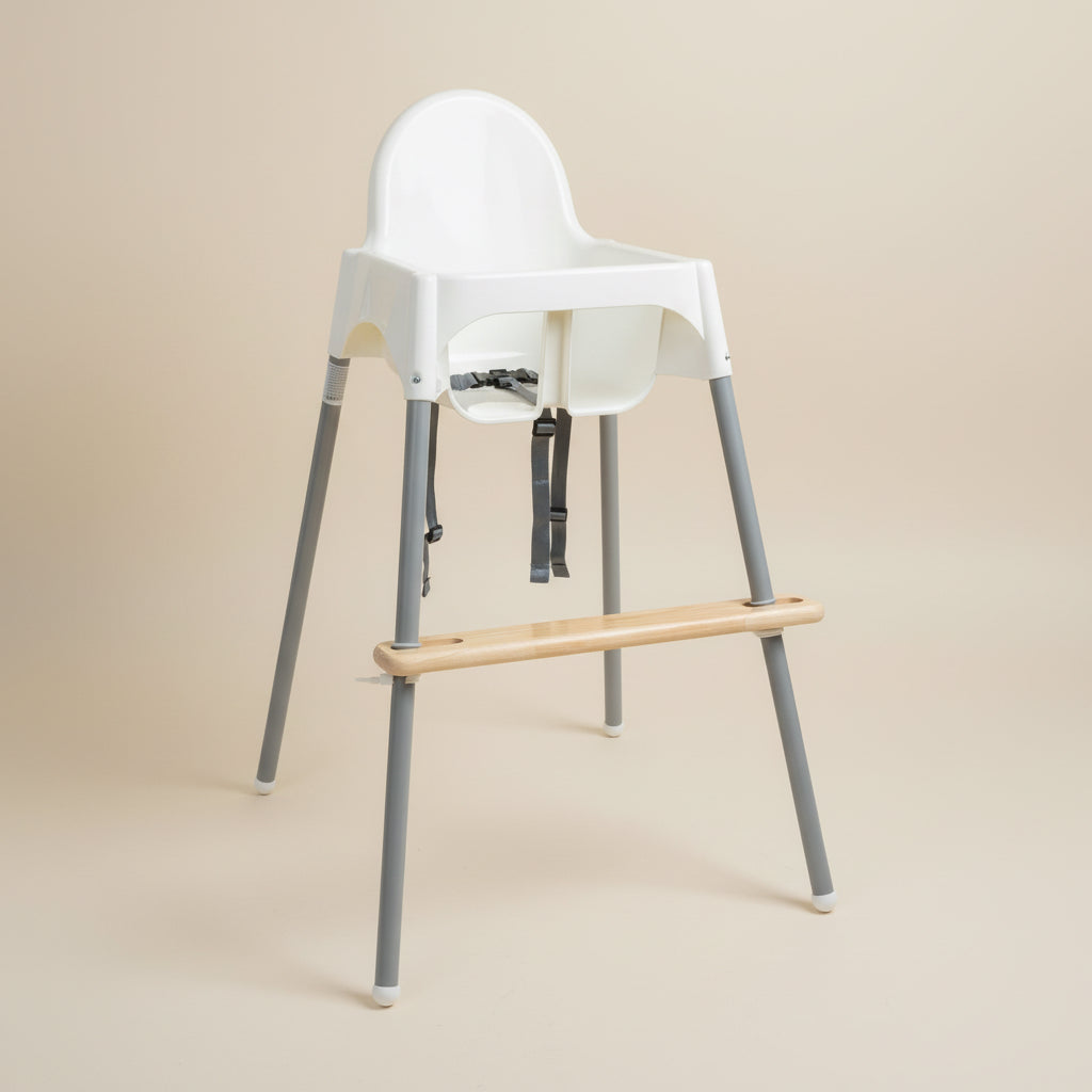 Child sitting on a white Ikea high chair with a footrest on a wooden floor.