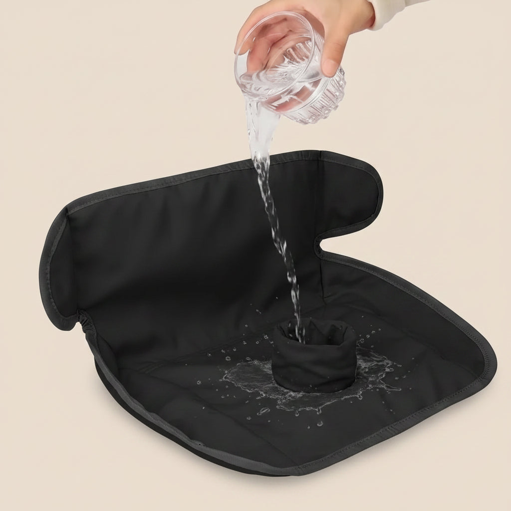 A black padded mat with black trim and a matching cup, shown with a hand pouring water from a glass into the center to demonstrate drainage.