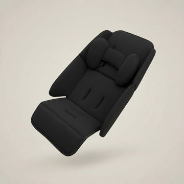 A black fabric car seat cushion with integrated headrest and side bolsters, shown floating against a plain warm beige background.