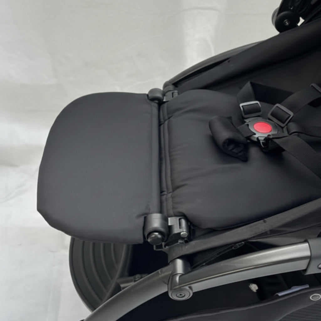 Close-up of a black stroller seat with a gray floor background