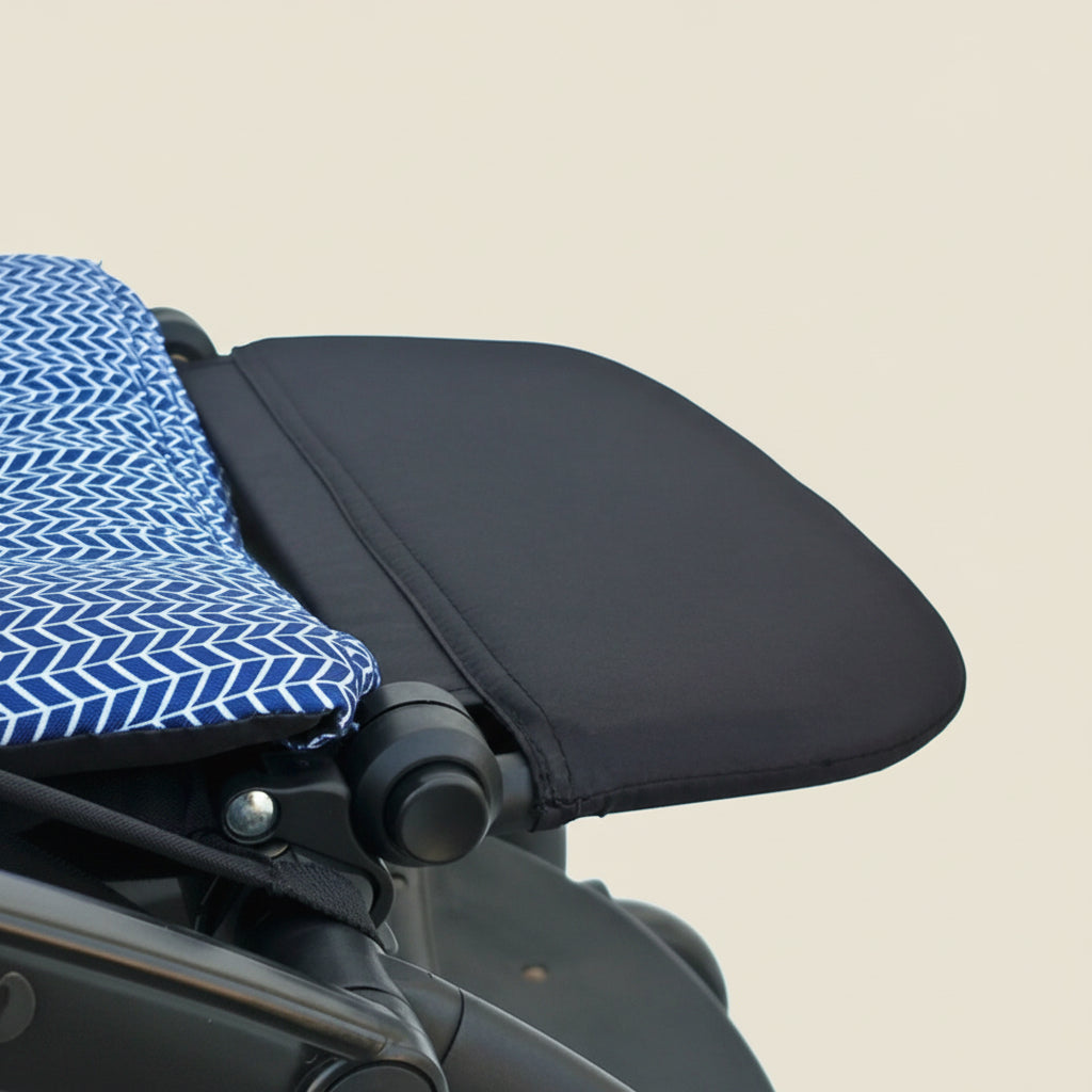 Close-up of a black stroller leg rest with a blue and white patterned cover on a white background